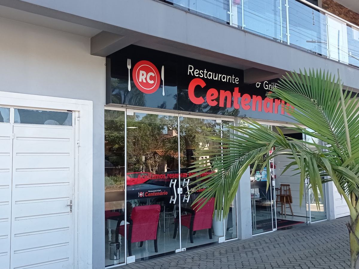 Fachada do Restaurante & Grill Centenário, com a placa vermelha e preta e a entrada de vidro.